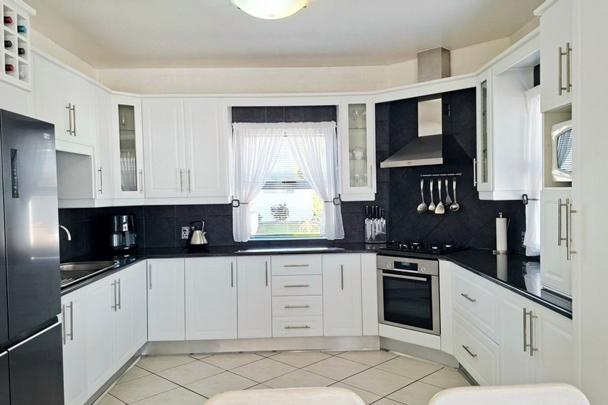A well-maintained kitchen featuring white cabinetry, black granite countertops, stainless steel appliances, and a tiled backsplash.