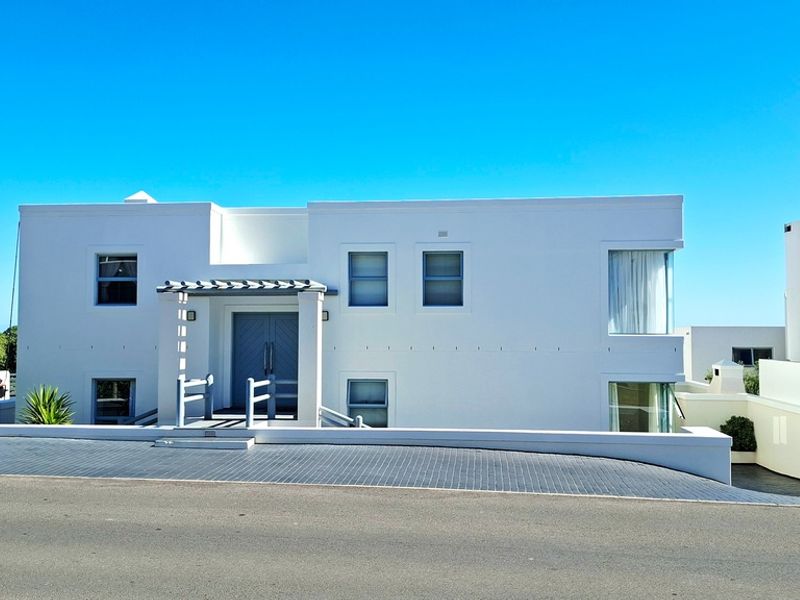 Modern white exterior facade featuring a paved driveway, a covered entrance with a pergola, and clean architectural lines.
