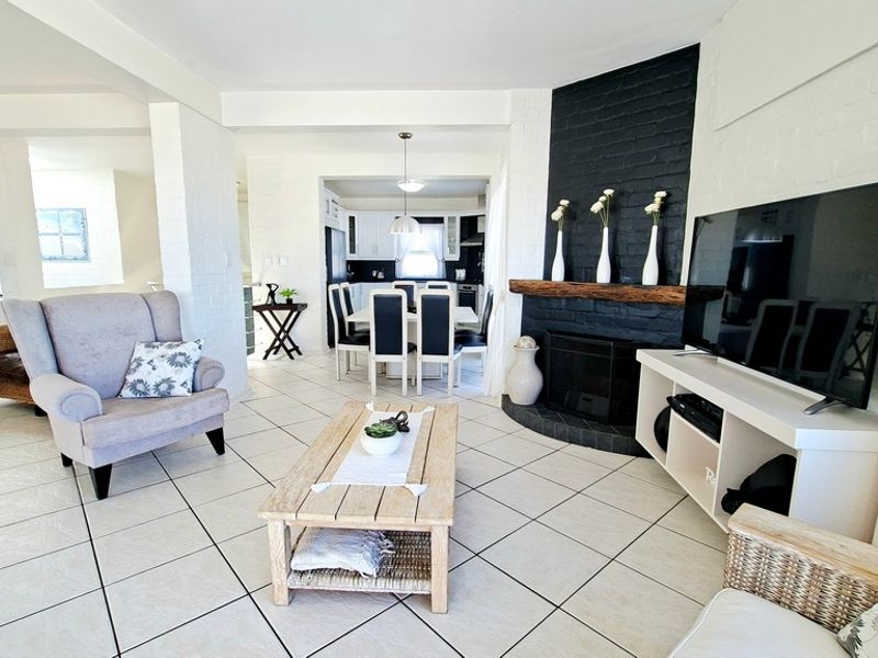 Spacious open-plan living and dining area featuring a prominent black brick fireplace with a timber mantelpiece and neutral tiled flooring throughout.