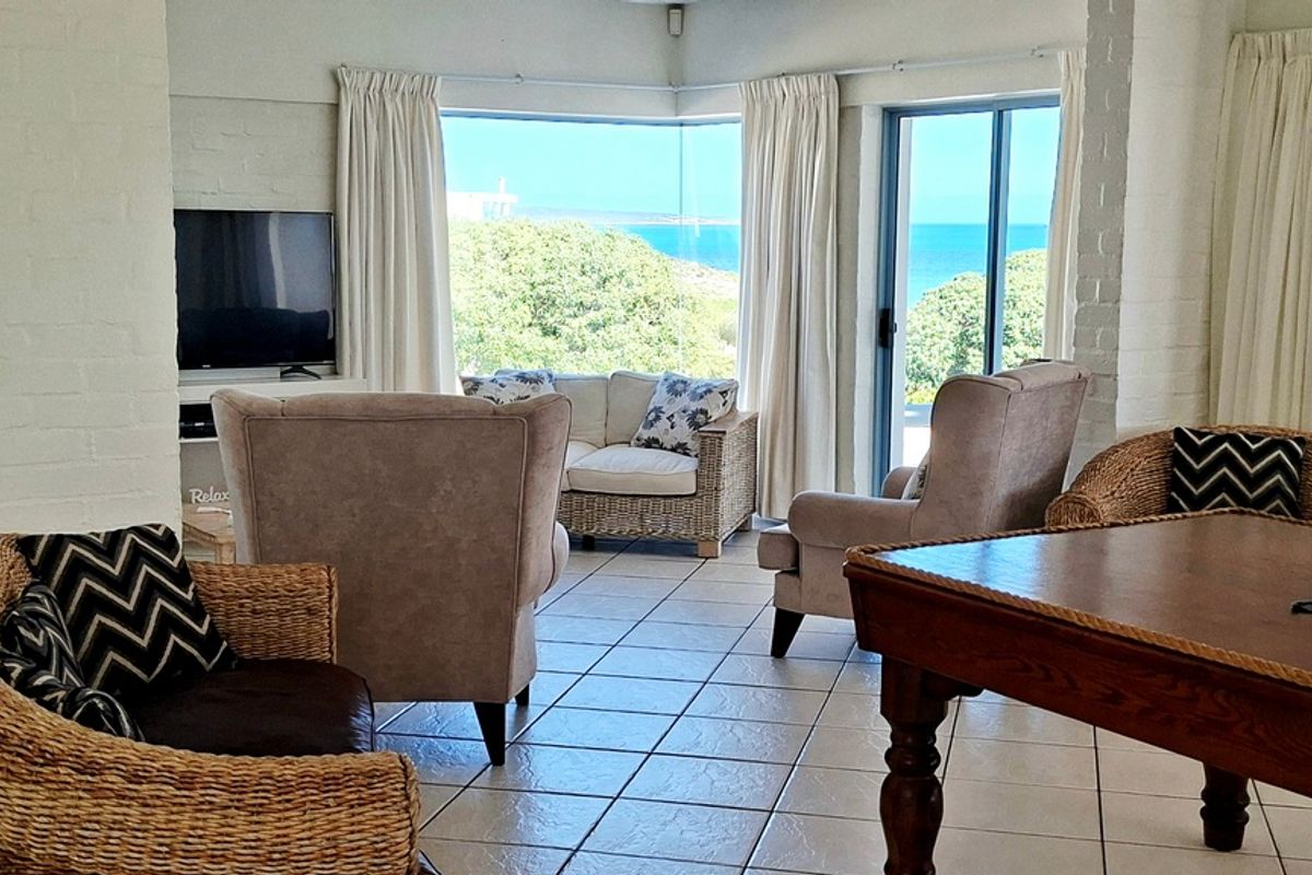 Bright living room featuring tiled flooring, painted brick walls, and a corner window with scenic ocean views and sliding door access to the exterior.