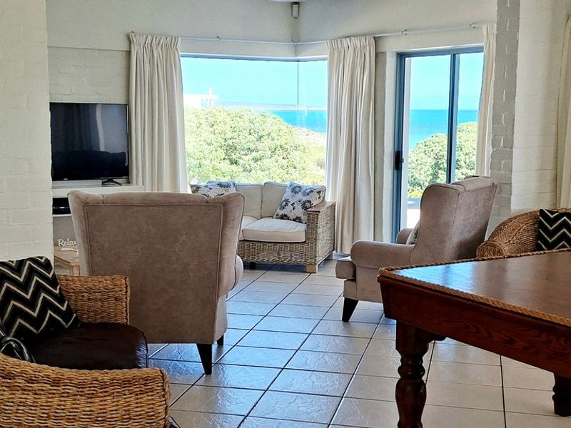 Bright living room featuring tiled flooring, painted brick walls, and a corner window with scenic ocean views and sliding door access to the exterior.