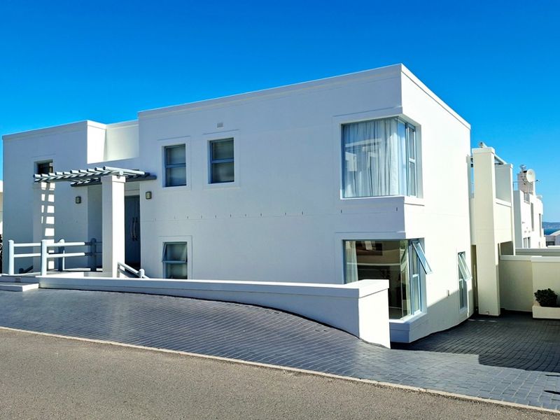 Modern two-story residential facade featuring clean white lines, corner windows, a paved driveway, and a welcoming pergola entrance.