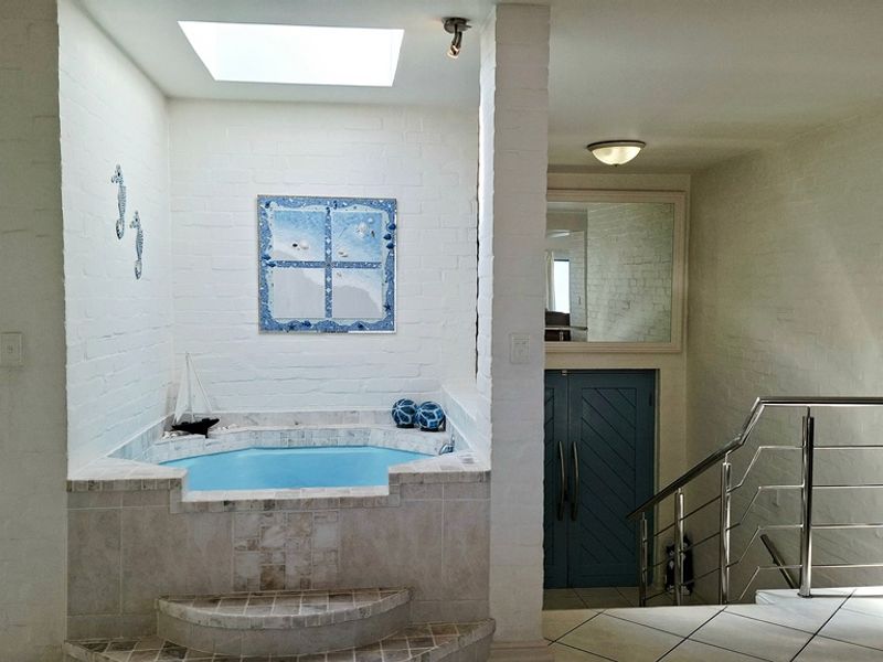 A unique bathroom area featuring a built-in spa bath under a skylight, complemented by tiled steps and a modern stainless steel staircase railing.