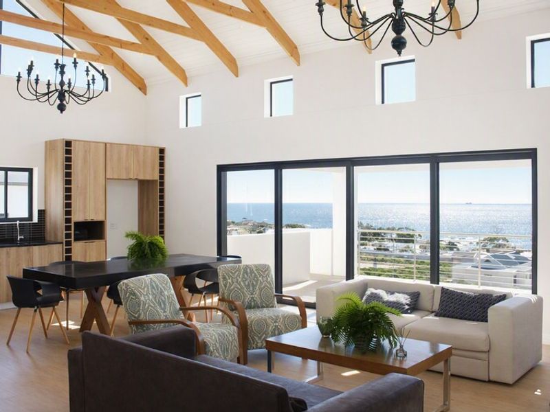 Spacious open-plan living area featuring vaulted ceilings with exposed timber trusses, modern built-in cabinetry, and large sliding doors opening to a scenic balcony.