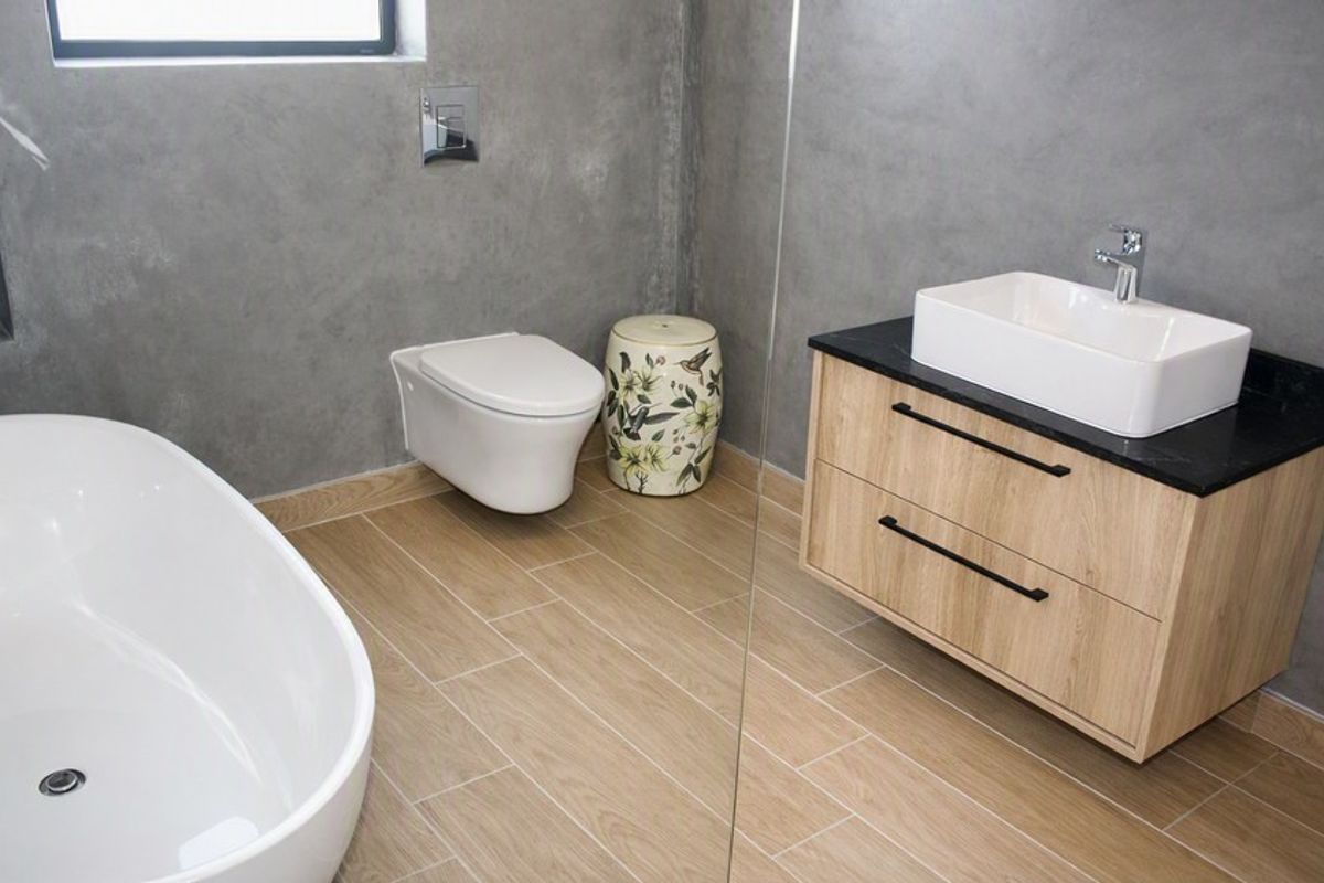 Modern bathroom featuring a freestanding bathtub, wall-mounted toilet, wood-look floor tiles, and a contemporary vanity with a vessel sink.
