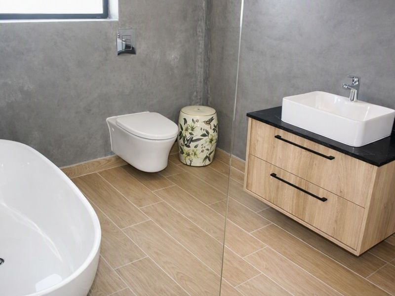 Modern bathroom featuring a freestanding bathtub, wall-mounted toilet, wood-look floor tiles, and a contemporary vanity with a vessel sink.