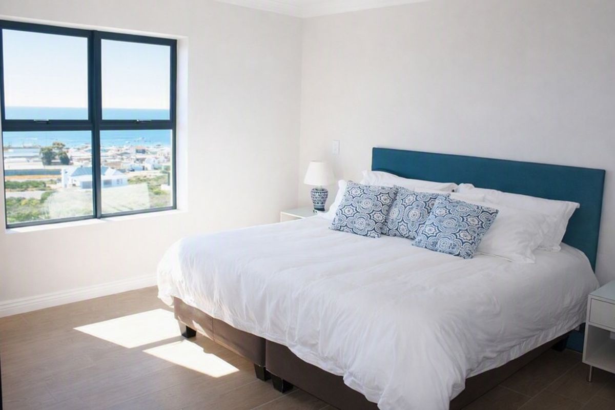 A bright and modern bedroom featuring neutral tiled flooring and a large window offering expansive coastal views.