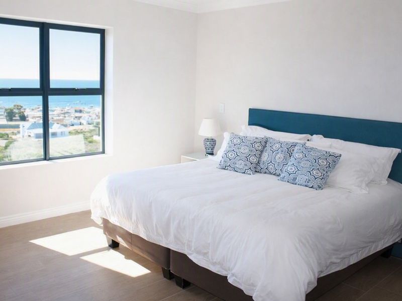 A bright and modern bedroom featuring neutral tiled flooring and a large window offering expansive coastal views.