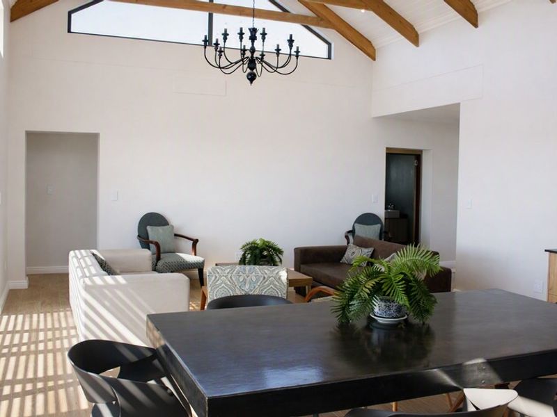 Spacious open-plan living and dining area featuring a vaulted ceiling with exposed timber beams, large sliding glass doors, and modern kitchen cabinetry.