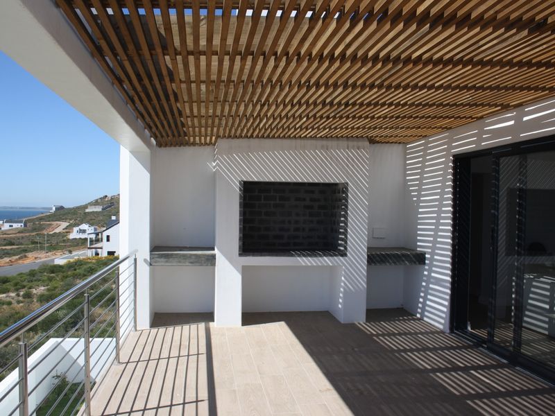 Covered balcony featuring a built-in braai, timber slat pergola, and stainless steel balustrade, offering expansive coastal views.