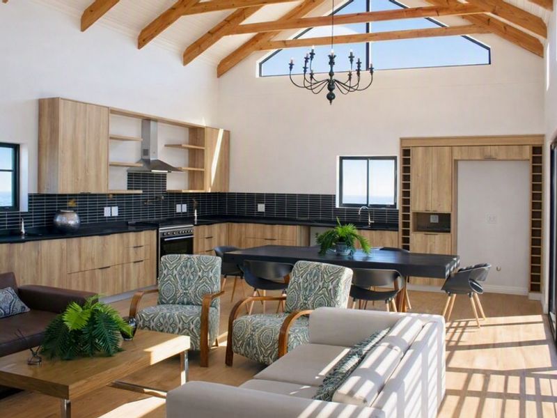 Spacious open-plan living and kitchen area featuring vaulted ceilings with exposed timber trusses, modern cabinetry, and large sliding doors leading to the exterior.
