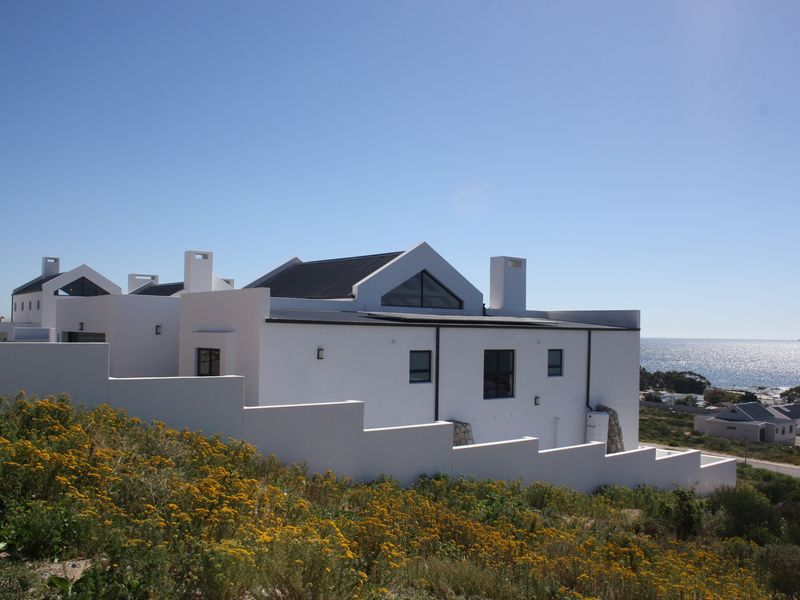 A modern white house with a pitched roof and chimneys, featuring a stepped boundary wall and scenic coastal views.