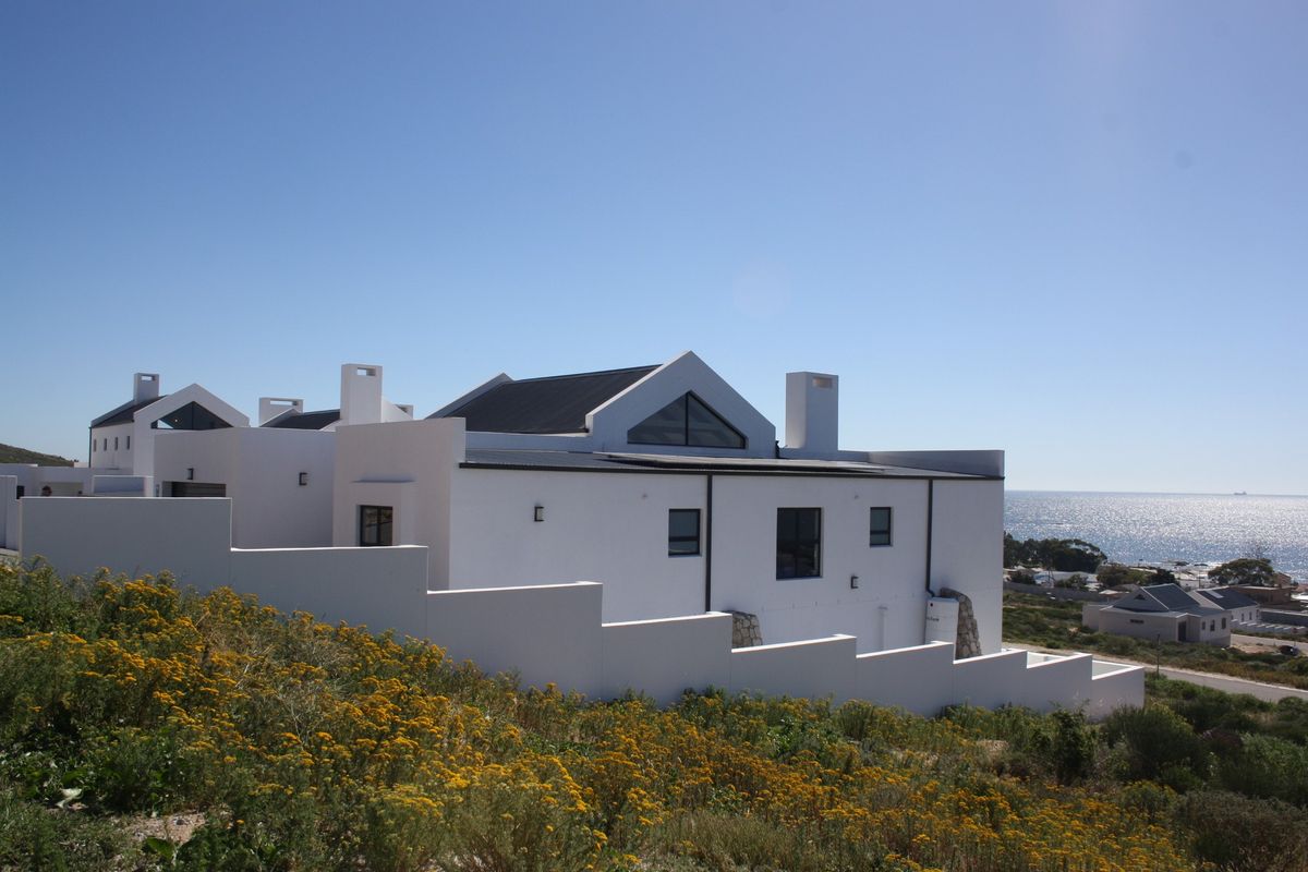 A modern white house with a pitched roof and chimneys, featuring a stepped boundary wall and scenic coastal views.