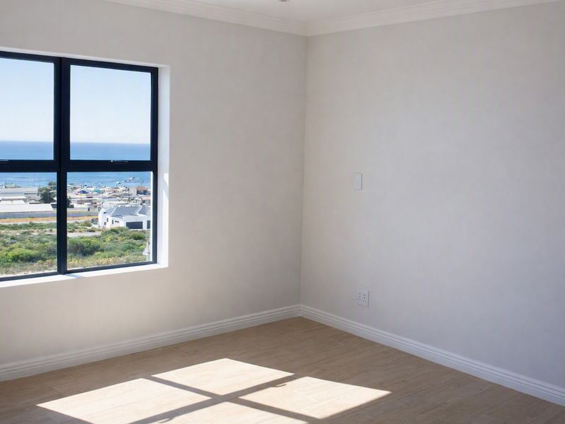 A bright, empty bedroom featuring modern laminate flooring, neutral walls, and a large window offering scenic coastal views.