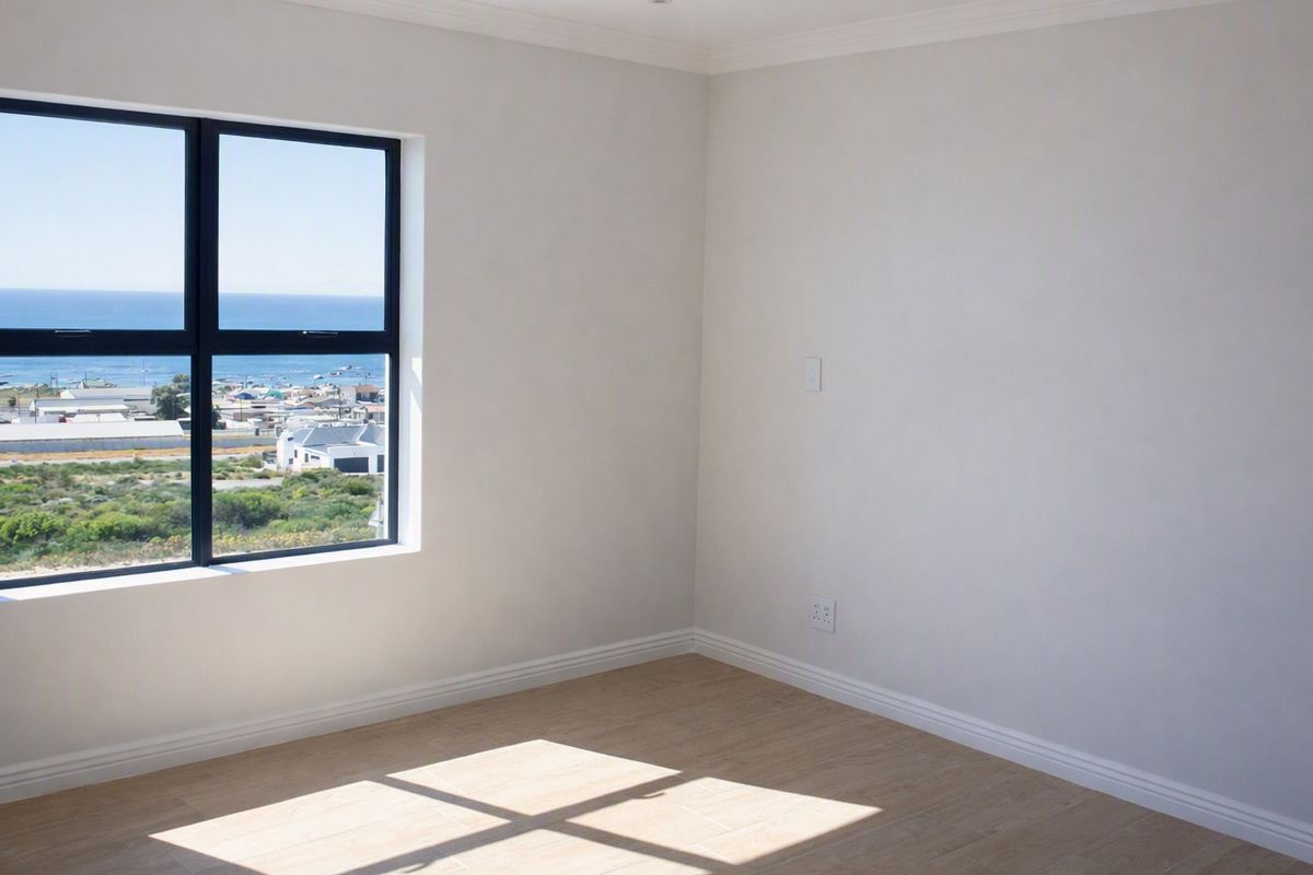 A bright, empty bedroom featuring modern laminate flooring, neutral walls, and a large window offering scenic coastal views.