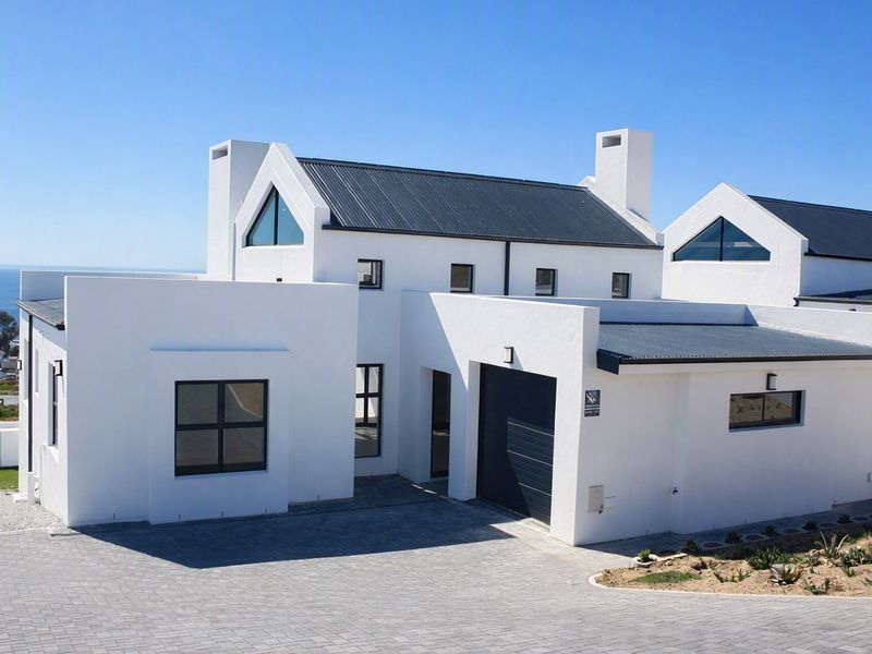 Modern white house with a metal roof, triangular windows, and a paved driveway, featuring a clean architectural design and ocean views.