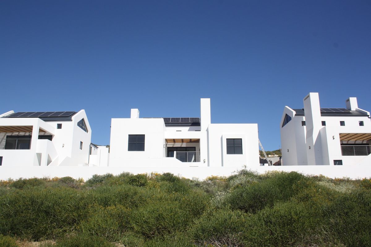 Rear view of modern white residential units featuring solar panels, timber pergolas, and clean architectural lines set against a clear blue sky.
