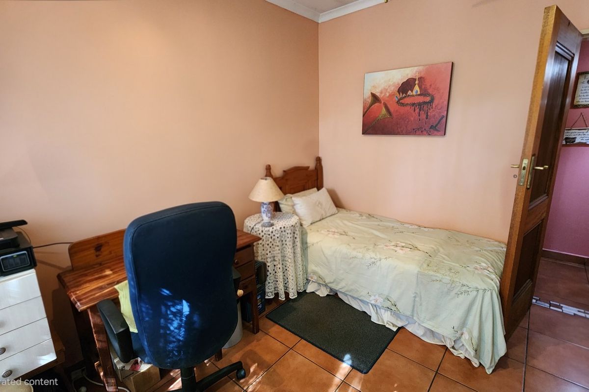 A compact bedroom featuring tiled flooring and a wooden door, currently utilized as a combined sleeping and workspace area.
