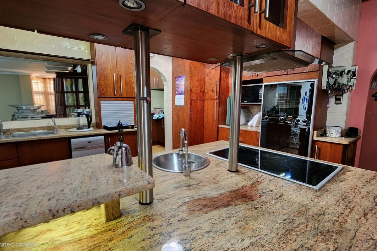 A spacious kitchen featuring a large granite-topped island with an integrated cooktop and sink, complemented by extensive wooden cabinetry and built-in appliances.