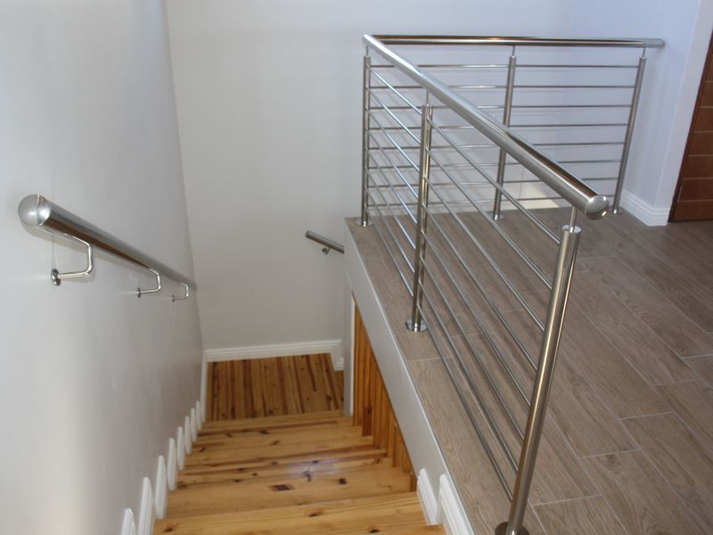 A modern staircase featuring timber treads, a sleek stainless steel balustrade, and a tiled landing area.