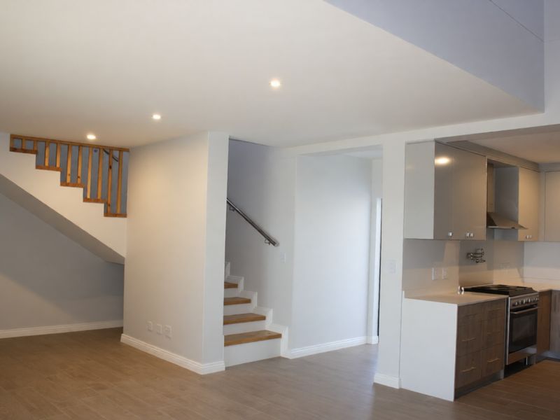 Modern open-plan living area featuring a sleek kitchen with built-in appliances and a staircase with wooden detailing.