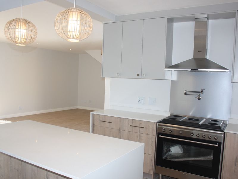 Modern open-plan kitchen featuring a central island, quartz countertops, stainless steel appliances, and sleek cabinetry, seamlessly flowing into an adjacent living area.