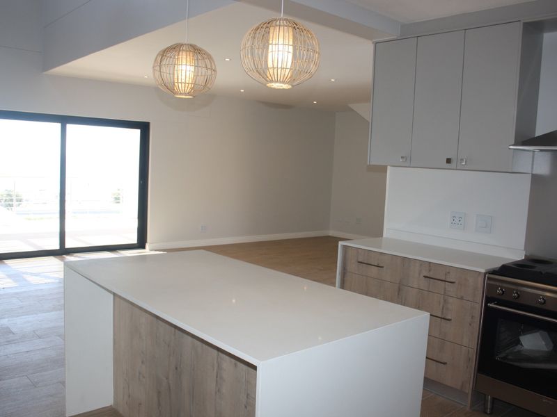Modern open-plan kitchen and living area featuring a central island, contemporary cabinetry, built-in oven, and large sliding doors leading to an outdoor space.