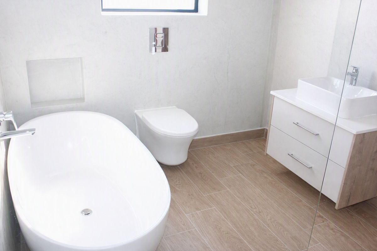 Modern bathroom featuring a sleek freestanding bathtub, wall-mounted toilet, and a contemporary vanity with a vessel sink and wood-look tile flooring.