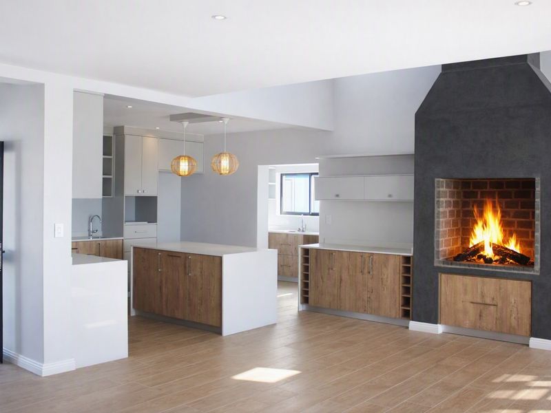 Spacious open-plan living area featuring a modern kitchen with island, scullery, and a striking built-in fireplace with a dark feature surround.