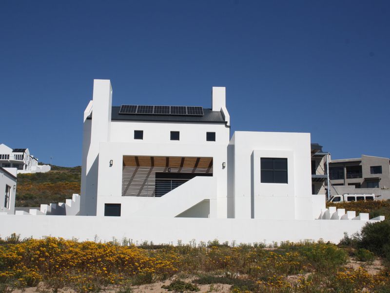 Modern white multi-level house exterior featuring a metal roof, integrated solar panels, and a covered patio area with an external staircase.