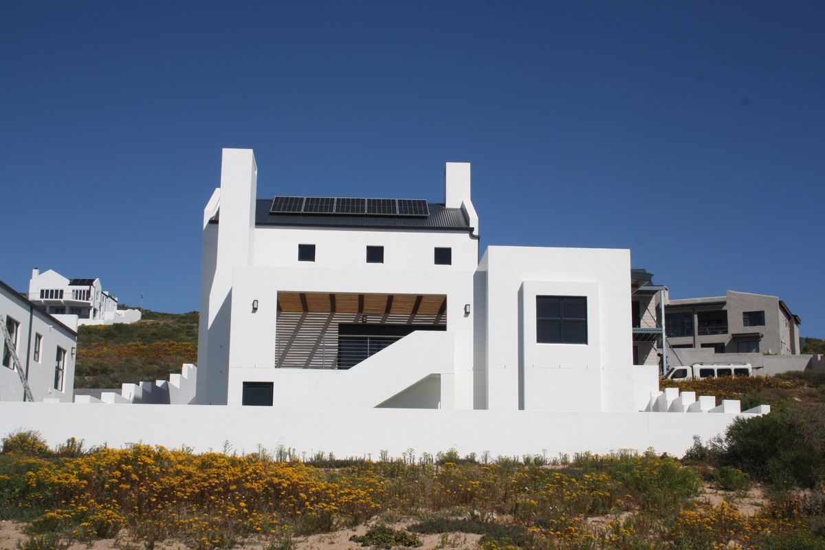 Modern white multi-level house exterior featuring a metal roof, integrated solar panels, and a covered patio area with an external staircase.