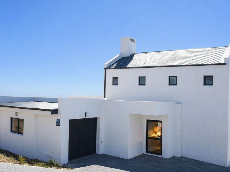 Modern white house with a corrugated metal roof, integrated garage, and paved driveway, featuring clean architectural lines and coastal views.