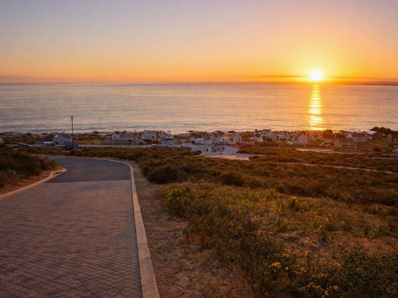 A scenic view of the coastline at sunset, featuring a paved driveway leading towards the ocean and surrounding residential area.