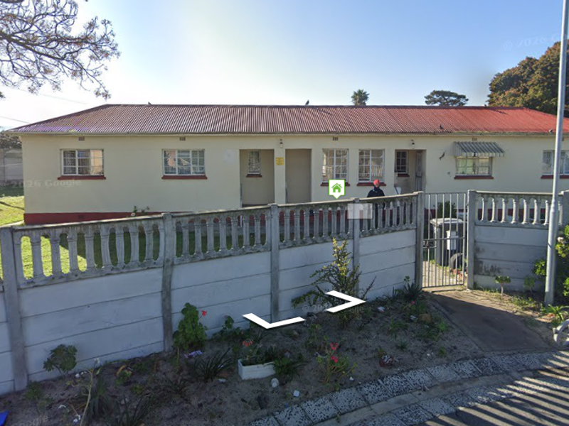 Front view of a single-story residential property featuring a corrugated metal roof, steel window frames, and a precast concrete boundary wall.