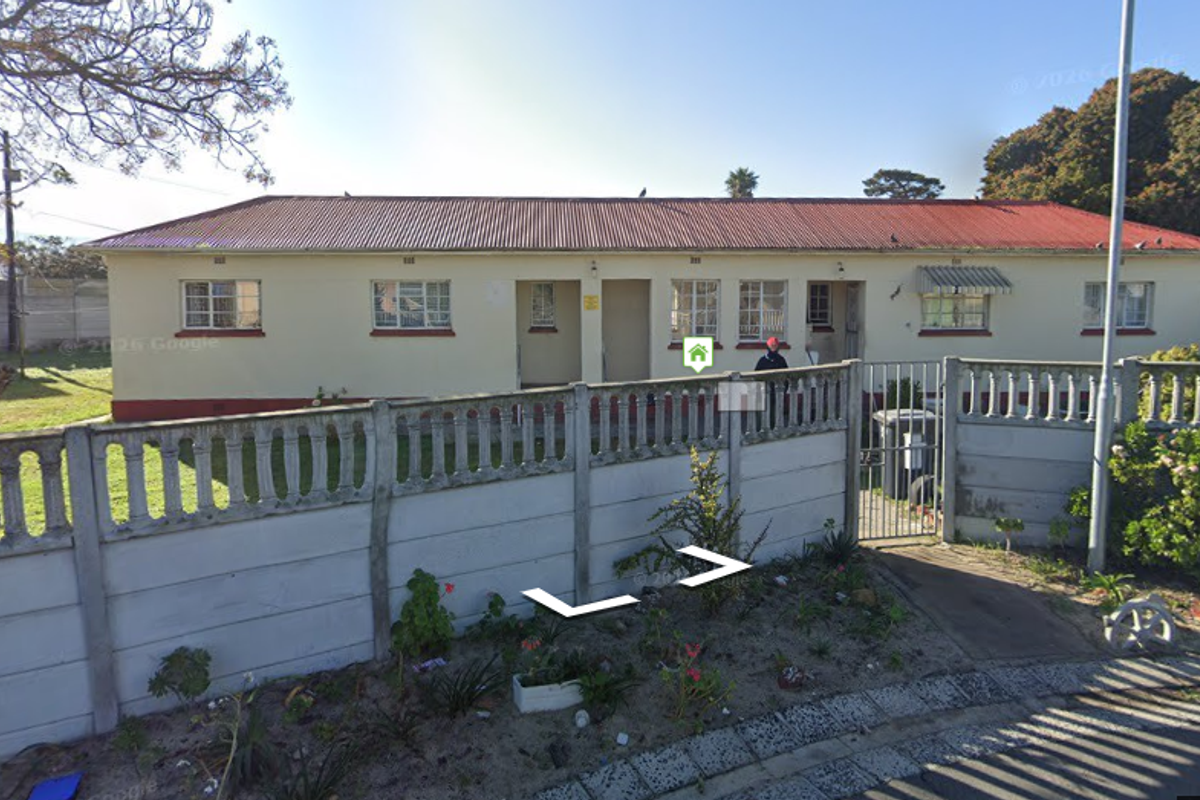 Front view of a single-story residential property featuring a corrugated metal roof, steel window frames, and a precast concrete boundary wall.