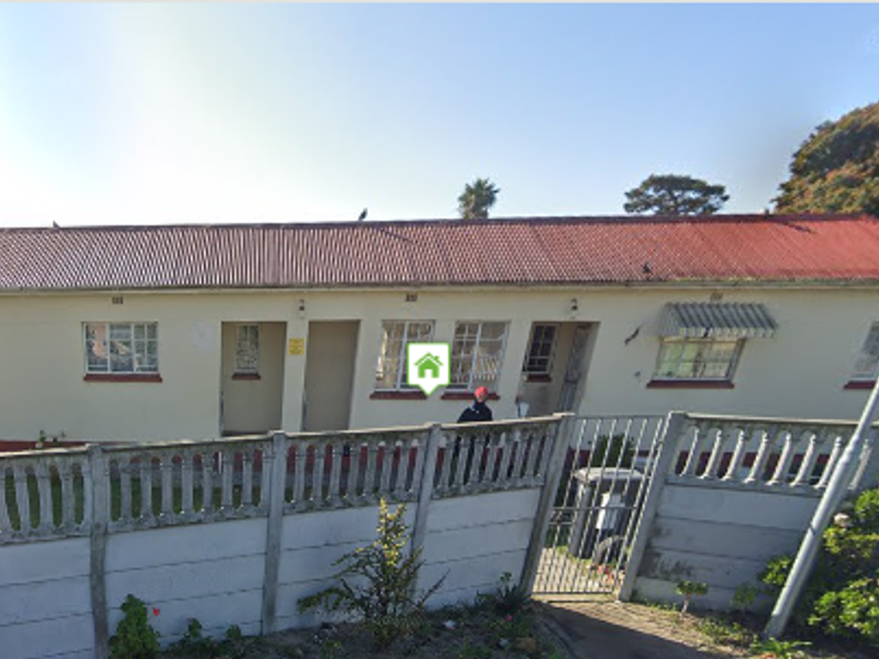 Front elevation of a single-story residential property featuring a corrugated metal roof, steel windows, and a precast concrete boundary wall.
