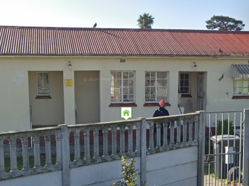 Front elevation of a single-story residential property featuring a corrugated metal roof, steel-framed windows, and a precast concrete boundary wall.