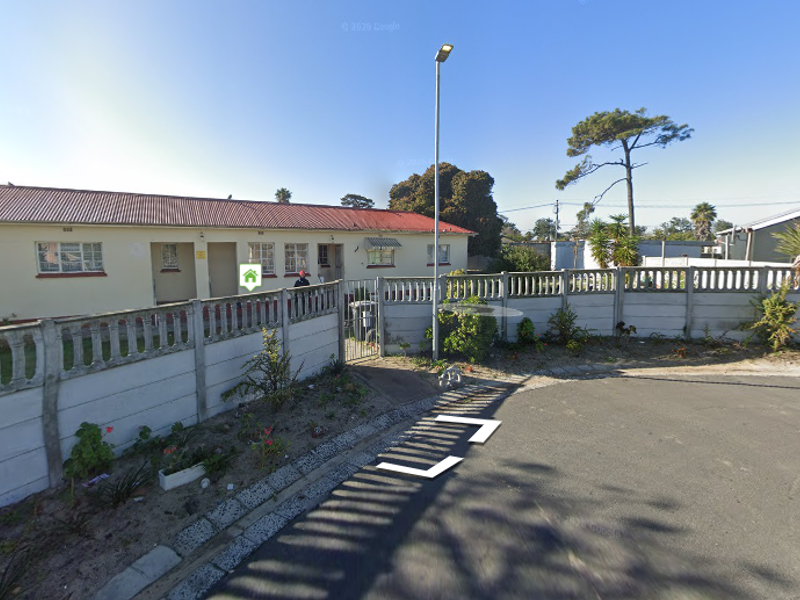 Front exterior view of a single-story residential property featuring a corrugated metal roof, security window bars, and a precast concrete boundary wall.