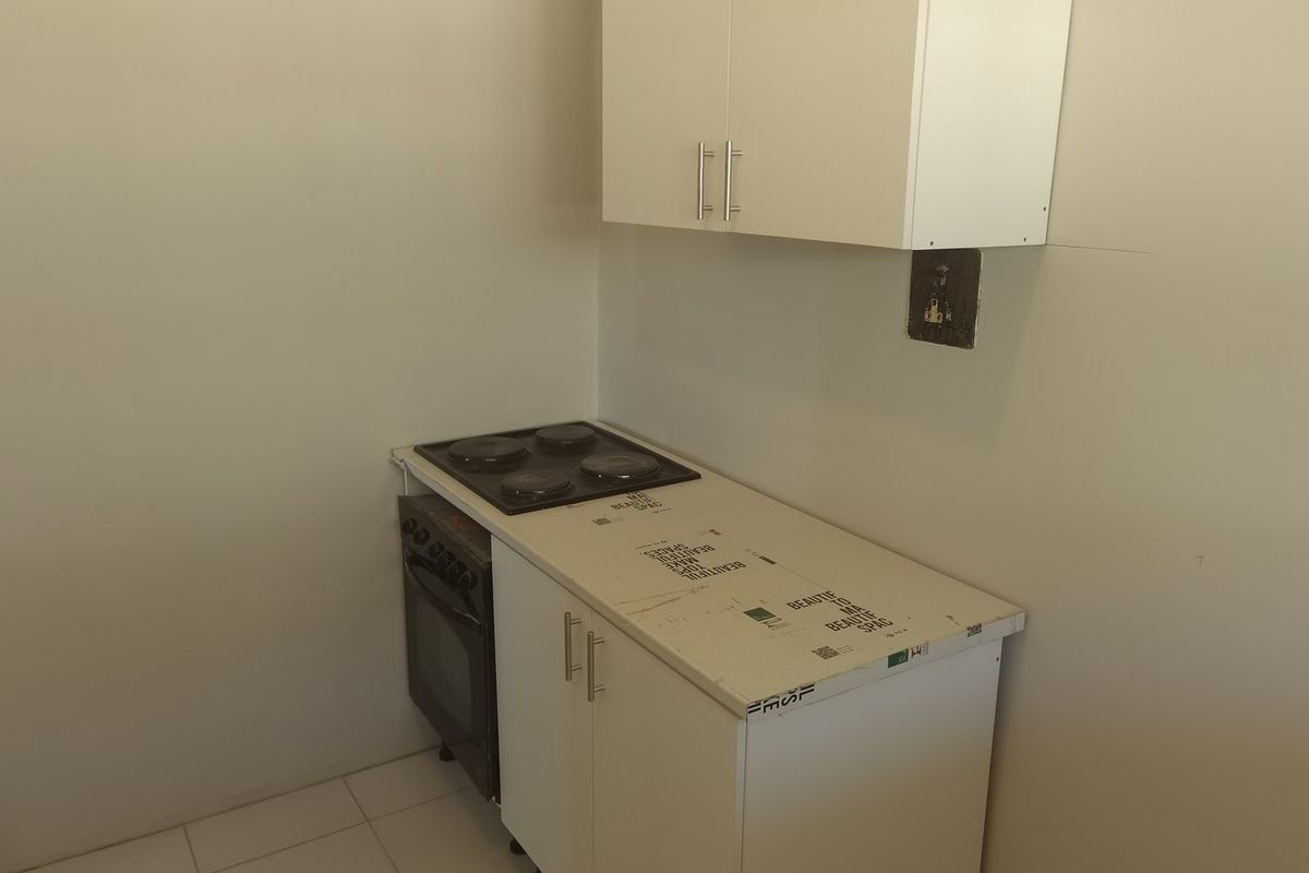 A compact kitchen area featuring white cabinetry, an integrated electric stove and oven, and tiled flooring, currently in a basic, unfinished state.