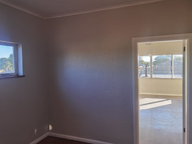 An empty bedroom featuring neutral walls, coving, and skirting boards, with a doorway leading to an adjacent sunroom or balcony area.