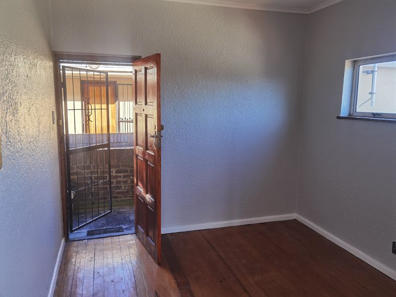 An empty bedroom featuring original wooden flooring, a timber door with a security gate, and a small window, offering a blank canvas for renovation.