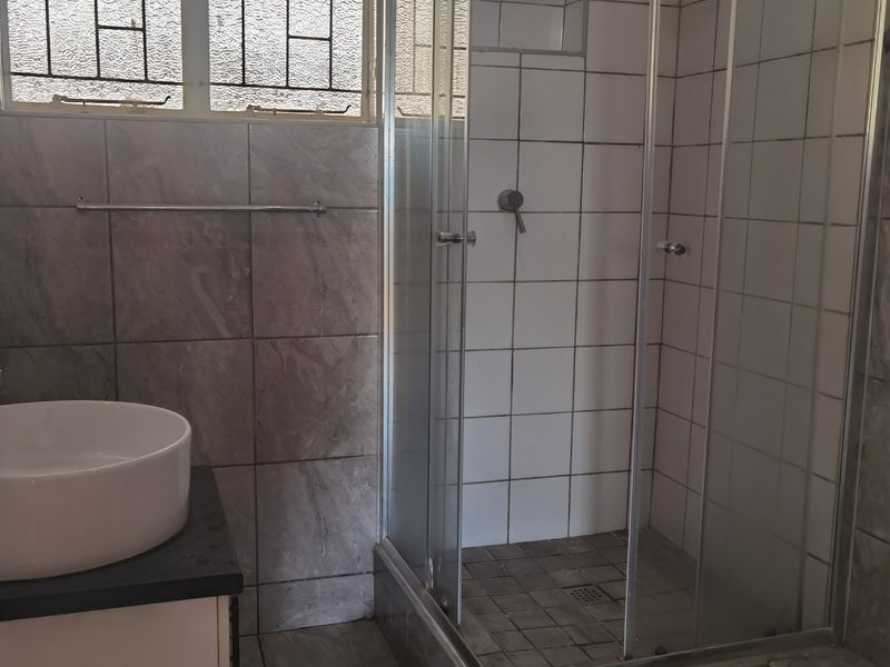 A functional bathroom featuring a glass-enclosed shower, a modern vessel sink on a vanity countertop, and tiled finishes throughout.