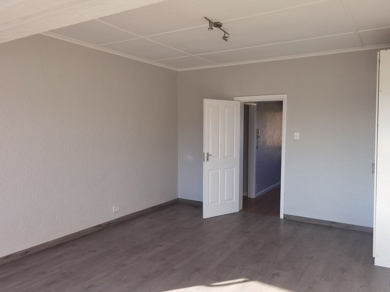 A spacious, empty bedroom featuring neutral grey walls, laminate flooring, and a built-in cupboard, offering a clean canvas for personalization.
