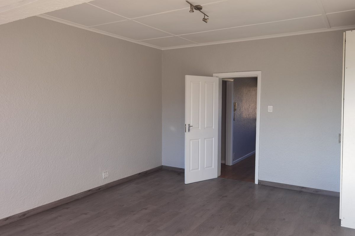A spacious, empty bedroom featuring neutral grey walls, laminate flooring, and a built-in cupboard, offering a clean canvas for personalization.
