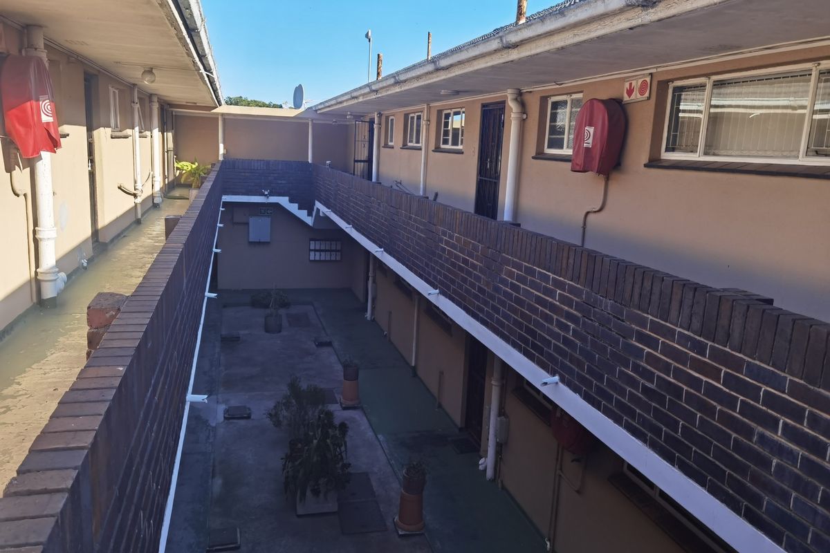 An exterior view of an apartment complex walkway featuring brick balustrades, concrete flooring, and access to multiple residential units.
