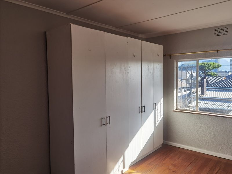 A bedroom featuring timber flooring and built-in cupboards, offering a functional space with natural light and views of the surrounding neighborhood.