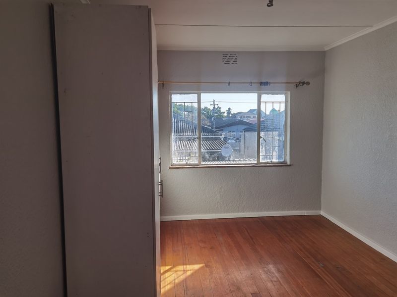 An empty bedroom featuring original timber flooring, a built-in wardrobe, and a window with security bars overlooking the neighborhood.