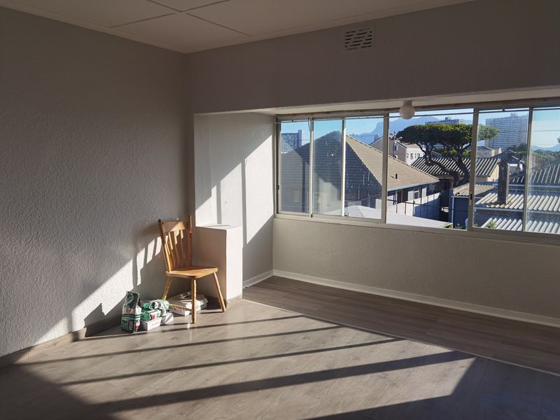 A bright, empty living area featuring modern laminate flooring and large windows that provide ample natural light and urban views.