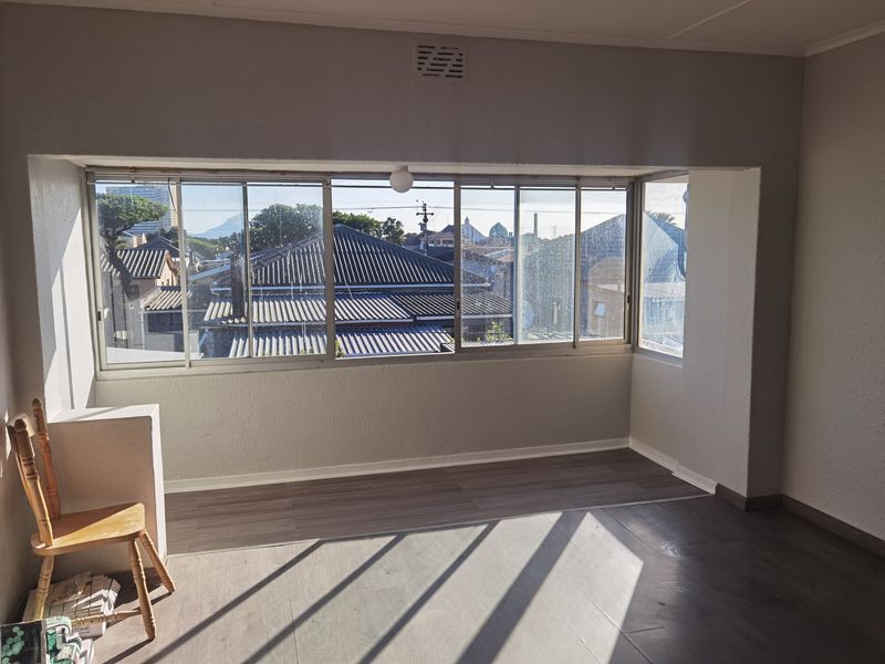 A bright, empty living area featuring modern laminate flooring and large sliding windows that provide ample natural light and neighborhood views.