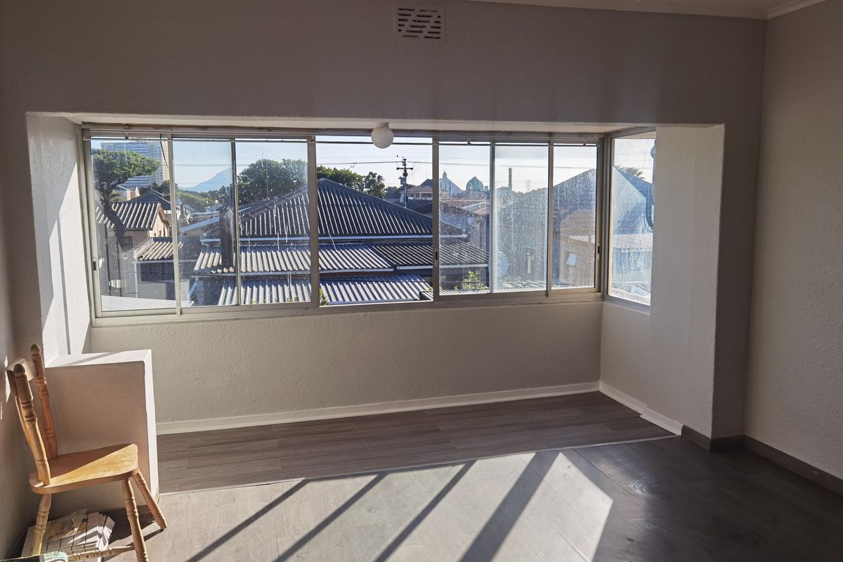 A bright, empty living area featuring modern laminate flooring and large sliding windows that provide ample natural light and neighborhood views.
